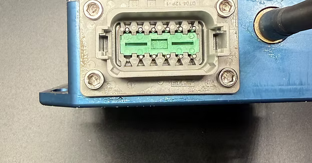 Close-up of X8Pro receiver's 12-pin connector plug on the aluminum housing, mounted with corner screws.